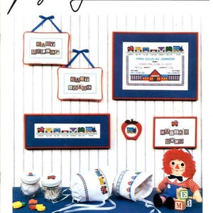 May include: A cross-stitch pattern booklet titled Imagining For Little Boys Booklet 10, featuring designs for wall hangings, framed birth announcements, train motifs, decorated jars, baby bonnets, and a rag doll with alphabet blocks.