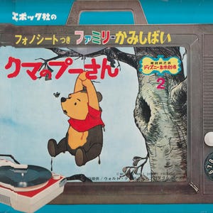 May include: A vintage record player with a Winnie the Pooh themed record. The record player is blue and white with a picture of Winnie the Pooh hanging from a tree branch. The text on the record player reads "エポック社の フォノシートつき ファミリーかみしばい クマプーさん ディズニー名作劇場 2".
