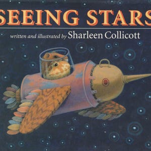 May include: A children's book cover with the title "SEEING STARS" written in orange and yellow letters. The book is written and illustrated by Sharleen Collicott. The cover features a cartoon illustration of two frogs in a spaceship flying through a starry night sky.