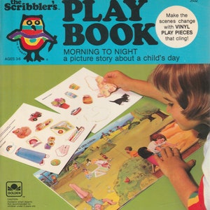 May include: A colorful book with a picture of an owl on the cover. The book is titled "The Scribbler's Play Book: Morning to Night, a picture story about a child's day." The book has a green background and the title is in black letters. The owl is colorful and has a rainbow pattern on its body. The book is open to a page with a picture of a child playing outside. The child is holding a vinyl sticker that they are placing on the page. The book is designed for children ages 3-6.