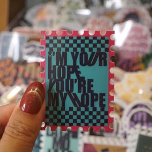 May include: A rectangular sticker with a perforated edge design, featuring a teal background with a black checkered pattern. The text "I'M YOUR HOPE YOU'RE MY HOPE" is printed in bold black letters across the center of the sticker.
