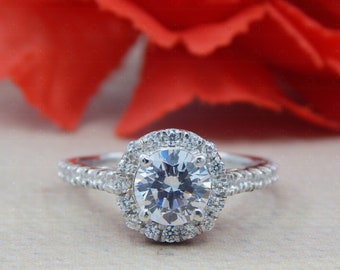 May include: A silver engagement ring with a large, round, clear center stone surrounded by a halo of smaller stones. The band is also set with smaller stones.