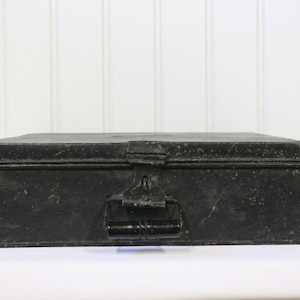 May include: A black metal box with a hinged lid and a metal handle. The box has a worn, distressed look.