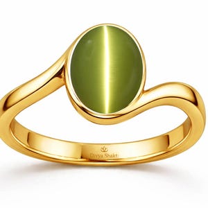 Op de afbeelding: Een gouden ring met een gladde, ovaalvormige olijfgroene kattenoog-edelsteen in een gepolijste band. De band heeft een gebogen ontwerp in bypass-stijl dat rond de steen loopt. De tekst Divya Shakti is gegraveerd op de binnenkant van de ring.
