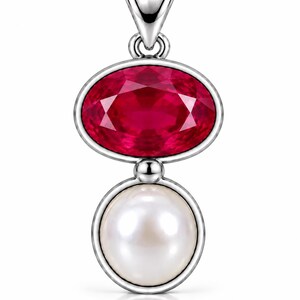 May include: A silver pendant featuring an oval-shaped, faceted deep red gemstone positioned above a round, white pearl. The two stones are set in a polished silver frame with a silver bail at the top for attachment to a necklace chain.