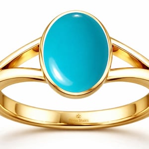 May include: A gold ring featuring a smooth, oval-shaped turquoise gemstone set in a polished yellow gold band with a split shank design. The interior of the band is engraved with the text Divya Shakti and a small lotus flower icon.
