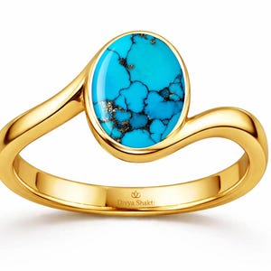 Op de afbeelding: Een gouden ring met een ovaalvormige turkoois edelsteen met donkere matrixaders. De ringband heeft een gladde, gepolijste afwerking en een bypass-ontwerp. De binnenzijde is gegraveerd met de tekst Divya Shakti en een klein lotus-icoontje.
