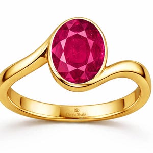 May include: A gold ring featuring a single oval-cut vibrant red gemstone set in a smooth bezel setting. The band has a curved, bypass-style design. The interior of the band is engraved with the text Divya Shakti and a small lotus flower icon.