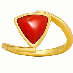 Puede incluir: Anillo dorado con una llamativa gema roja triangular. La gema está engastada en un marco dorado, y la banda del anillo tiene un diseño curvo y fluido. Una pieza de joyería elegante.