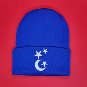 May include: A blue knitted beanie with a white crescent moon and stars design.
