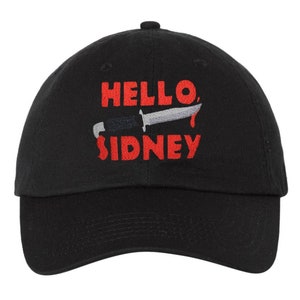 May include: Black baseball cap with red embroidered text that reads "HELLO, SIDNEY" with a knife graphic above the text.