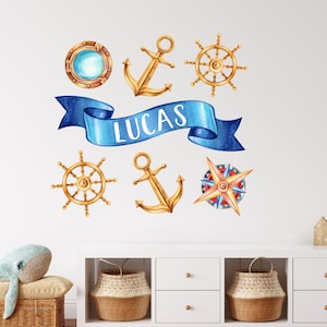 Könnte beinhalten: Ein blaues Banner mit dem Namen "Lucas" in weißen Buchstaben, umgeben von nautischen Aufklebern. Die Aufkleber beinhalten einen Kompass, Anker, ein Bullauge und Steuerräder.