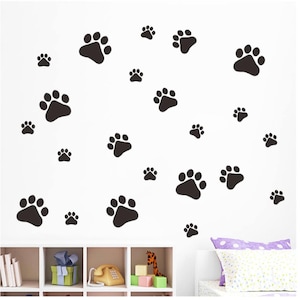 May include: Black paw print wall decals, a set of 20, arranged in a random pattern on a white wall. The decals are in various sizes and are perfect for adding a playful touch to a child's room or a pet-lover's home.