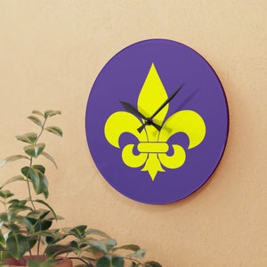 May include: A purple round clock with a yellow fleur-de-lis design. The clock hands are black.