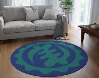 May include: A round rug with a blue background and a green Adinkra symbol in the center. The symbol is surrounded by a blue ring with a green border.
