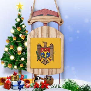 May include: A wooden Christmas sleigh ornament featuring a yellow, blue and red coat of arms on the front. The coat of arms depicts a golden eagle with a crescent moon and a star above it. The sleigh is decorated with a red ribbon and a gold star.
