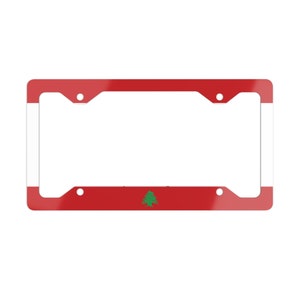 May include: A red, white and green licence plate frame featuring the flag of Lebanon. The frame has a white border and two holes on each side for mounting.