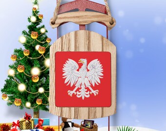 Op de afbeelding: Een houten kerstversiering in de vorm van een slee met een rood-witte Poolse vlag aan de voorkant. De vlag toont een witte adelaar op een rode achtergrond.