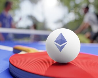 May include: A white ping pong ball featuring the Ethereum logo sits on a red ping pong bat. The bat rests on a blue table. Two people are playing table tennis in the background.