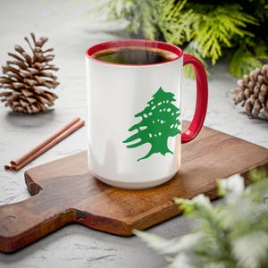 May include: White ceramic coffee mug with a red rim and handle. The mug features a green cedar tree design, the national symbol of Lebanon.