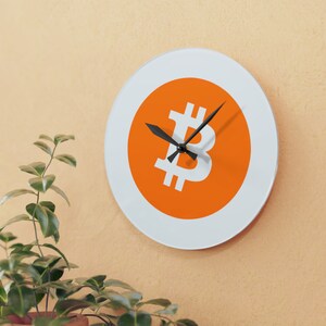 May include: A white circular clock with a black face and hands. The clock face features a large orange circle with a white Bitcoin symbol in the center.