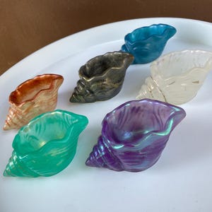 以下が含まれることがあります： オレンジ、緑、青、紫など、さまざまな色の貝殻型の装飾品が7つ。白い表面に配置され、詳細な螺旋模様が特徴です。