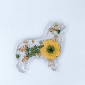 May include: A clear resin dog-shaped keychain with a pressed yellow sunflower and gold leaf accents.