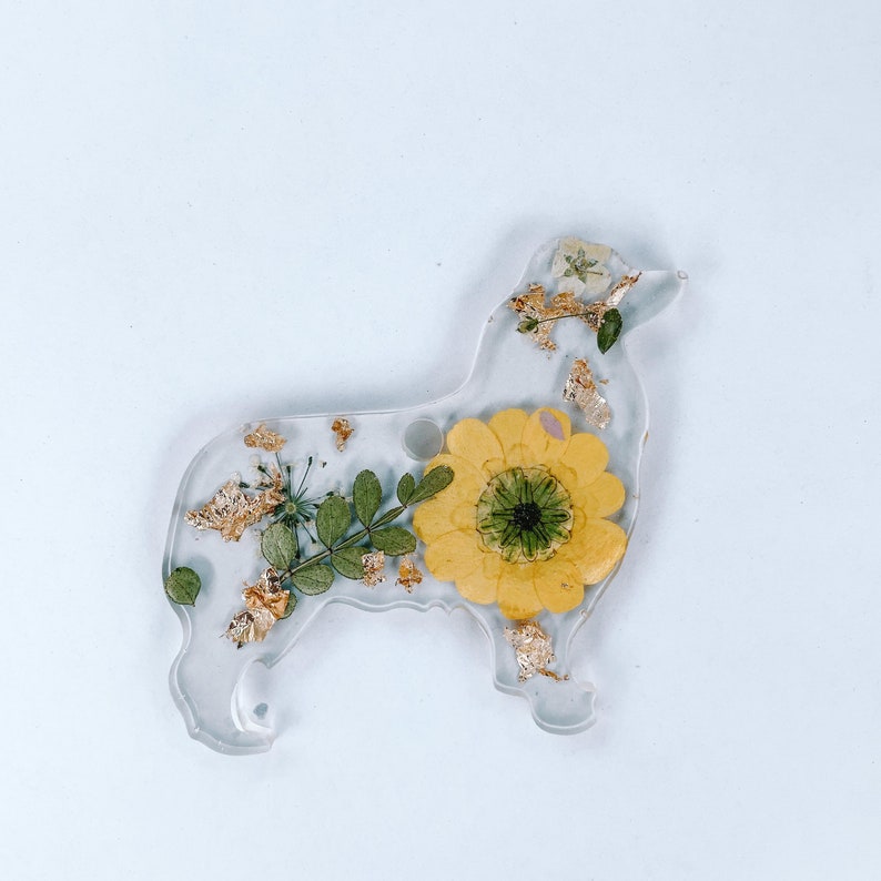 May include: A clear resin dog-shaped keychain with a pressed yellow sunflower and gold leaf accents.
