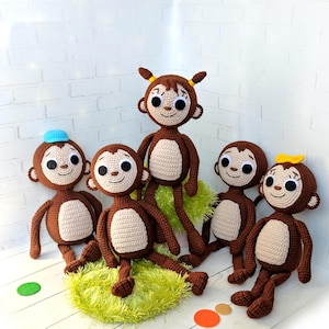 May include: Five brown crocheted monkey plushies with embroidered faces. The monkeys are sitting on a green fuzzy surface. One monkey is wearing a blue hat, another is wearing a yellow bow, and another has yellow yarn hair.