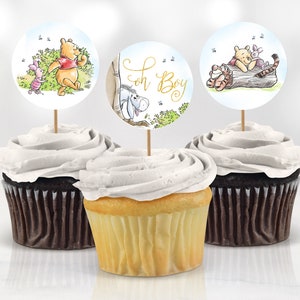 May include: Three Winnie the Pooh themed cupcake toppers featuring images of Winnie the Pooh, Piglet and Eeyore. The toppers are on cocktail sticks and are ready to be placed on cupcakes. One topper has the text "Oh Boy" on it.