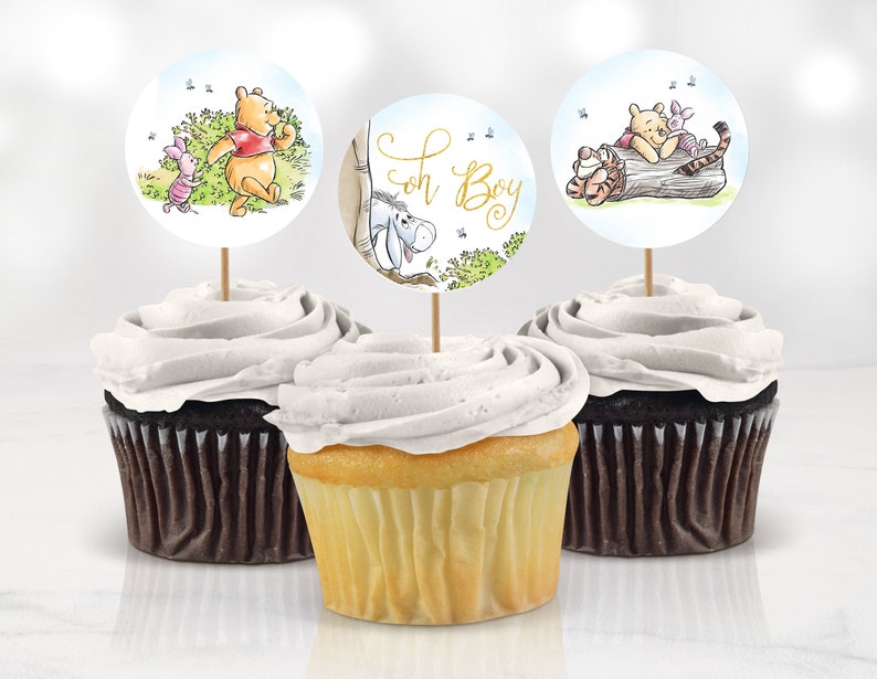 May include: Three Winnie the Pooh themed cupcake toppers featuring images of Winnie the Pooh, Piglet and Eeyore. The toppers are on cocktail sticks and are ready to be placed on cupcakes. One topper has the text "Oh Boy" on it.