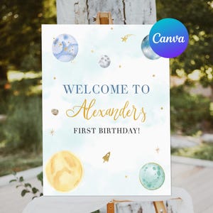 Puede incluir: Un cartel de bienvenida azul y blanco con letras doradas que dice "Bienvenido a Alexanders First Birthday!" El cartel presenta una ilustración de acuarela de planetas y estrellas.