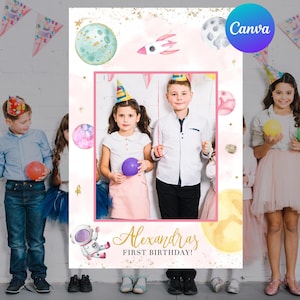 Puede incluir: Fondo de cabina de fotos para el primer cumpleaños con temática espacial rosa y dorado con un recorte para una foto. El fondo presenta planetas, estrellas, un cohete y un astronauta. El texto "Alexandra's First Birthday!" está escrito en letras doradas.