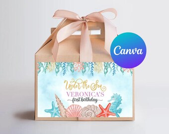 May include: A brown paper gift box with a light pink ribbon. The box features a watercolor design with the text "Under the Sea" and "Veronica's first birthday". The design includes seashells, a seahorse, and a starfish.