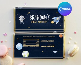 May include: A blue and gold chocolate bar wrapper with a space theme. It features an astronaut, a rocket, stars, and planets. The text on the wrapper reads "Brandon's First Birthday".