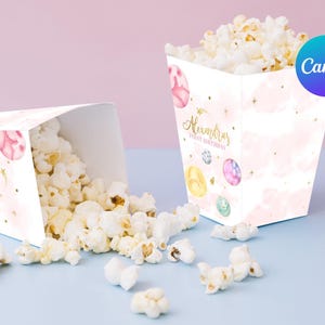 Puede incluir: Cajas de palomitas de maíz rosas y blancas con un diseño de acuarela de planetas y estrellas. Las cajas están decoradas con purpurina dorada y el texto "Alexandra's First Birthday".
