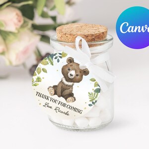 May include: A small glass jar filled with white sweets and tied with a white ribbon. A round tag with a green and gold leafy design and a cartoon brown bear is attached to the jar. The tag reads "Thank you for coming Love, Ricardo".