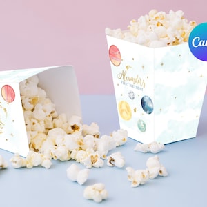 Puede incluir: Dos cajas de palomitas blancas con un fondo de acuarela azul y blanco y estrellas doradas. Las cajas tienen el texto "Alexander's First Birthday". Las cajas están llenas de palomitas y están sobre una superficie azul claro.