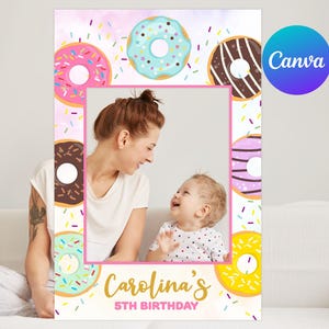 May include: A pink and white photo booth prop with a donut theme. The prop has a large cutout in the center for a photo. The prop is decorated with colorful donuts and sprinkles. The text "Carolina's 5th Birthday" is at the bottom of the prop.