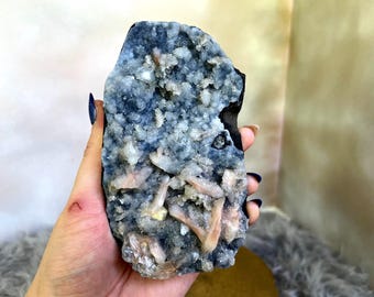 May include: A large, irregularly shaped crystal cluster. The crystal features a dark blue base with a textured surface, covered in small, white and peach-colored crystal formations. The overall appearance is rough and natural.