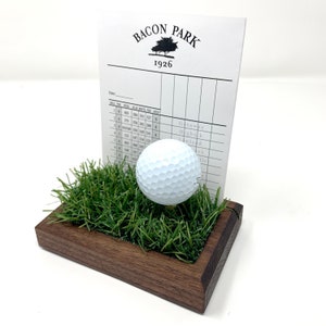 The golf scorecard a ball display holder is a handcrafted walnut display designed to showcase a golf ball and scorecard from your personal best round or hole-in-one. Featuring realistic fake grass under the golf ball on a tee, it’s a perfect way to commemorate your golfing achievements. Ideal for Father's Day, graduations, retirements, or golf trips, this unique gift is a stylish addition to any golfer’s home or office and makes a thoughtful gift for golf enthusiasts.
