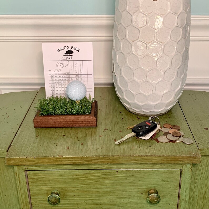 The golf scorecard a ball display holder is a handcrafted walnut display designed to showcase a golf ball and scorecard from your personal best round or hole-in-one. Featuring realistic fake grass under the golf ball on a tee, it’s a perfect way to commemorate your golfing achievements. Ideal for Father's Day, graduations, retirements, or golf trips, this unique gift is a stylish addition to any golfer’s home or office and makes a thoughtful gift for golf enthusiasts.