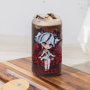 May include: A clear glass tumbler with a red and white illustration of a cartoon character with the text "CAMELLYA". The tumbler is filled with a dark liquid and ice cubes. A clear plastic straw and a wooden lid are also included.