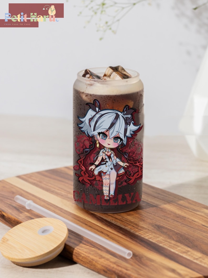 May include: A clear glass tumbler with a red and white illustration of a cartoon character with the text "CAMELLYA". The tumbler is filled with a dark liquid and ice cubes. A clear plastic straw and a wooden lid are also included.