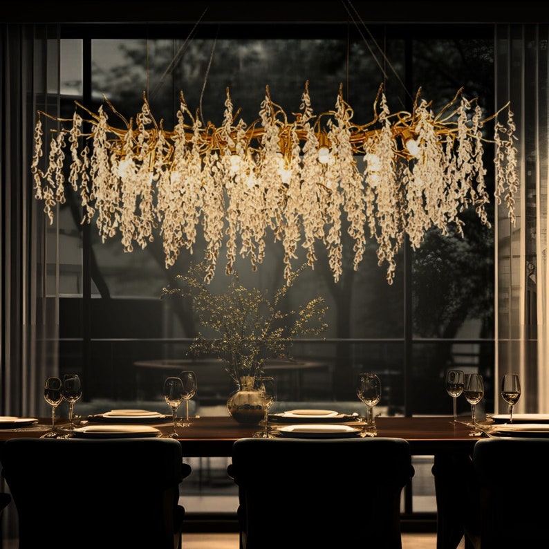 May include: A gold chandelier with crystal drops hangs over a dining table set with glasses and plates. The chandelier is shaped like a branch with cascading crystals.