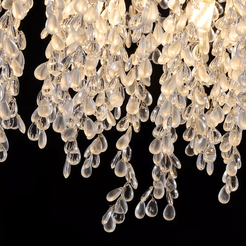 May include: Close-up of a crystal chandelier with many clear teardrop-shaped crystals hanging from a gold frame.