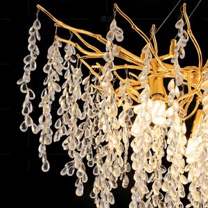 May include: A gold-toned chandelier with a unique branch-like design. The chandelier is adorned with cascading crystal teardrop-shaped pendants.