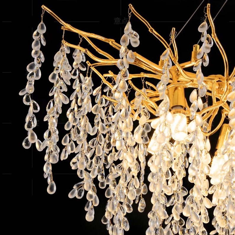 May include: A gold-toned chandelier with a unique branch-like design. The chandelier is adorned with cascading crystal teardrop-shaped pendants.