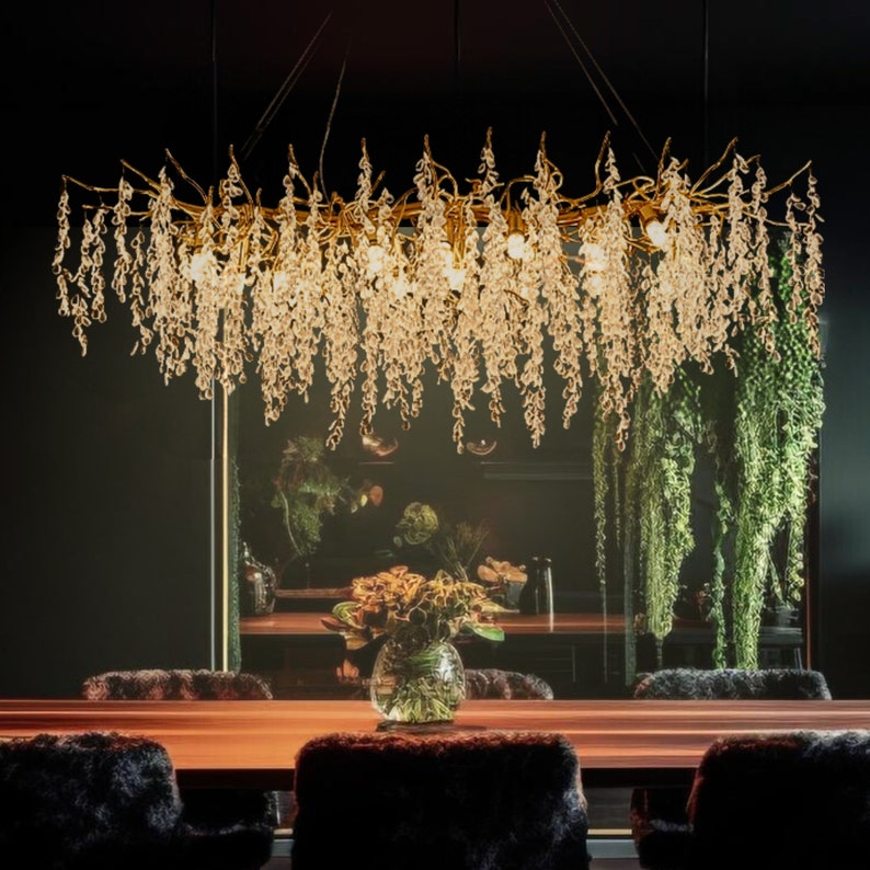 May include: A gold chandelier with crystal drops hanging from a branch-like frame. The chandelier is illuminated and casts a warm glow. The chandelier is hanging over a wooden table with chairs.