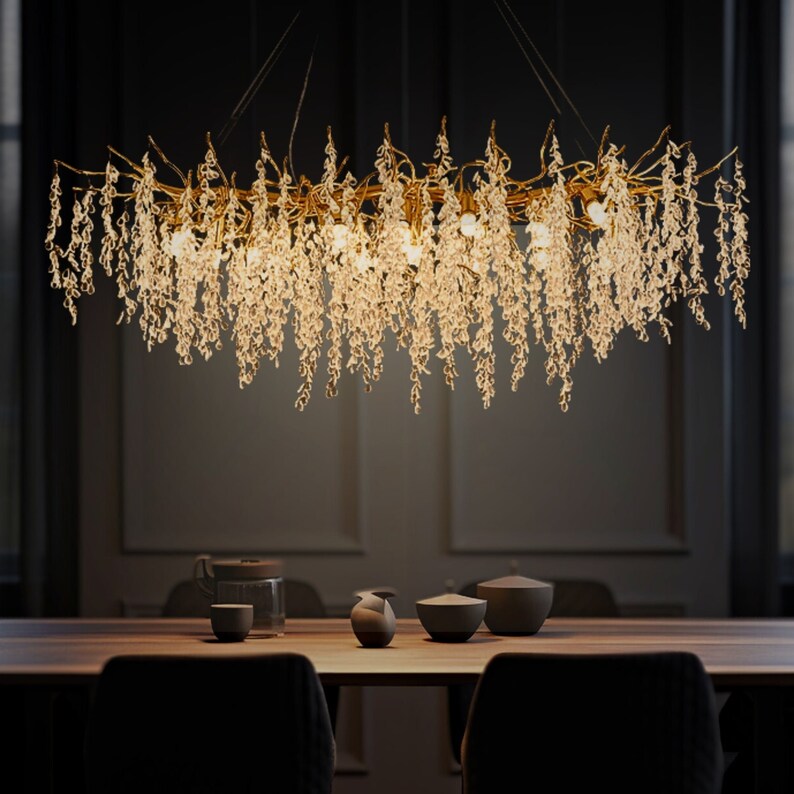 May include: A gold chandelier with crystal drops hanging from a branch-like frame. The chandelier is lit and casting a warm glow.